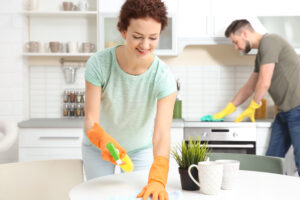 Ilustração de uma mulher e um homem limpando a cozinha juntos. Ambos estão com luvas laranjas.