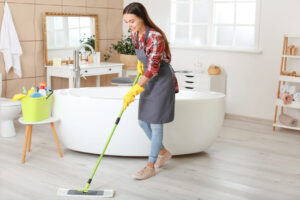 Ilustração de uma mulher limpando o piso de um banheiro aberto com um mop e Gel Limpa Banheiro